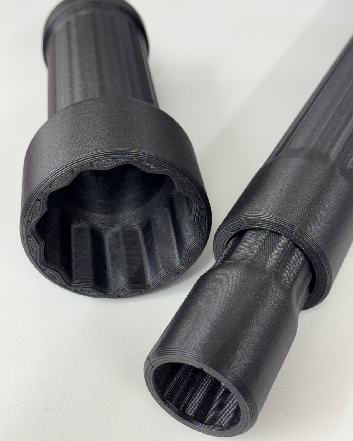 Two black 3D-printed tube wrenches on a white surface, showing fine layer detail and a matte machined-looking finish.